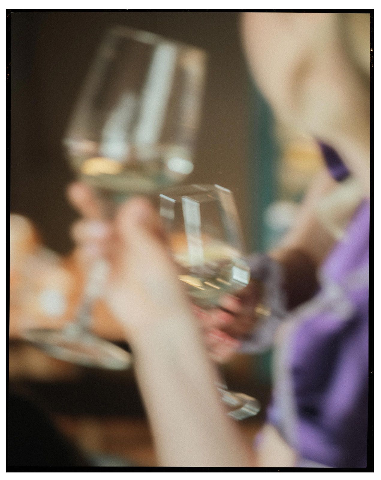Two people toasting with elegant wine glasses filled with white wine at a social gathering.