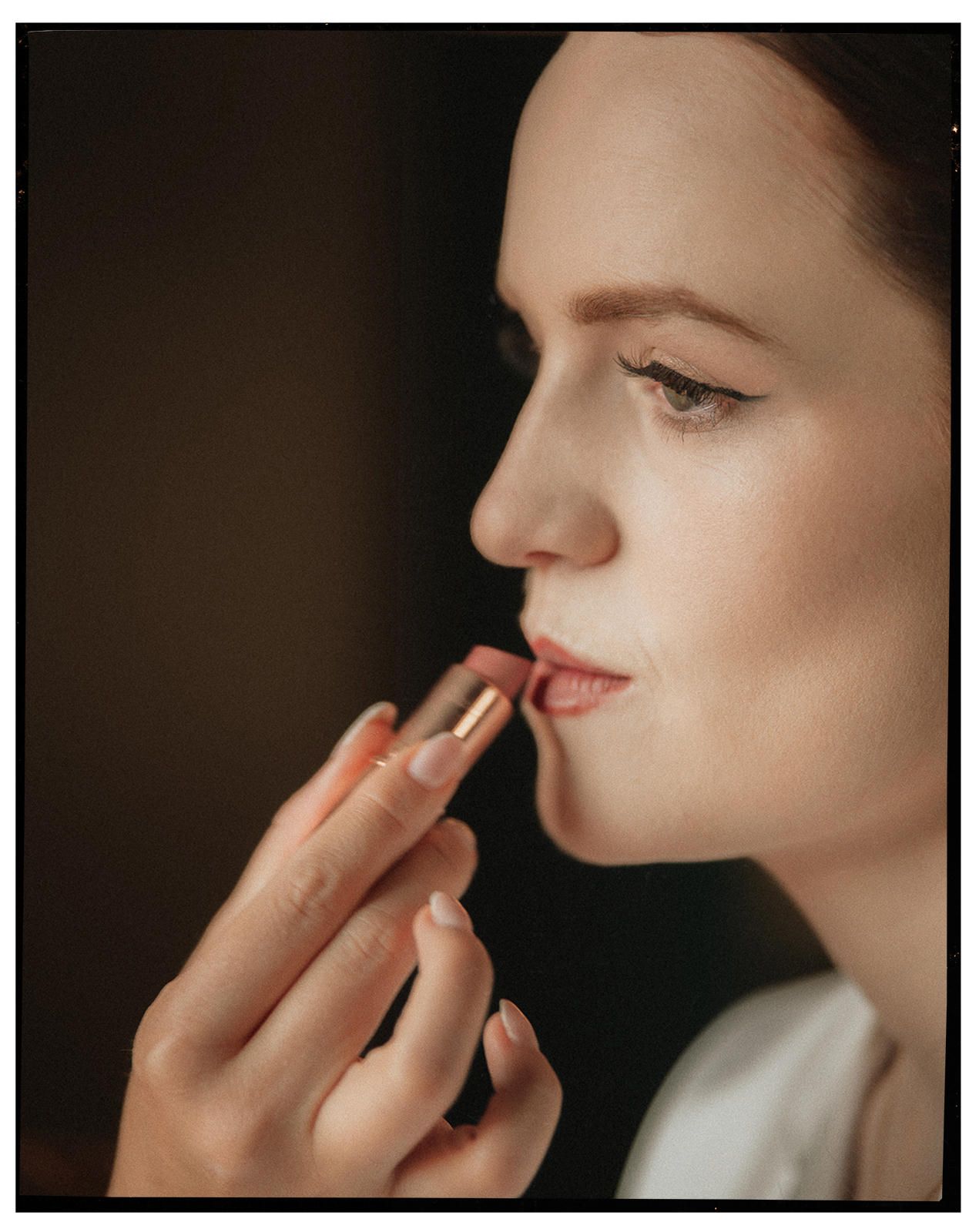 Close-up profile of a woman applying lipstick during bridal makeup preparation.