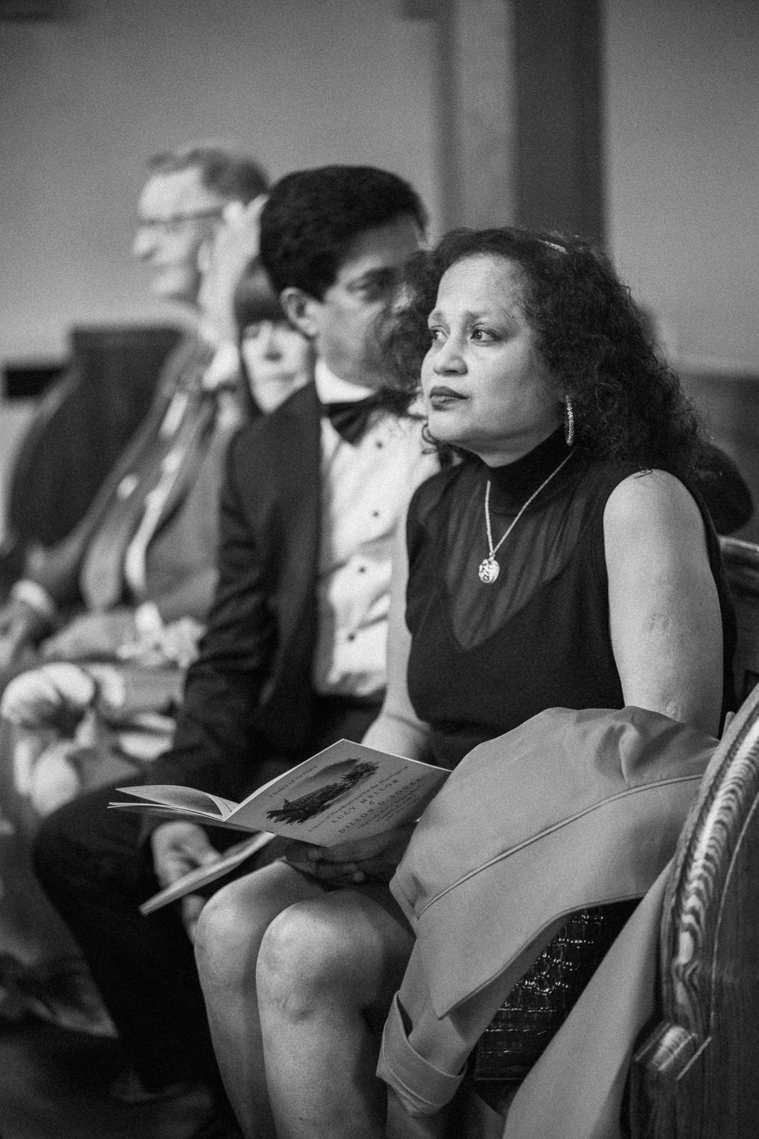 Black and white photo of wedding guests seated in chairs, woman in foreground holding a program.