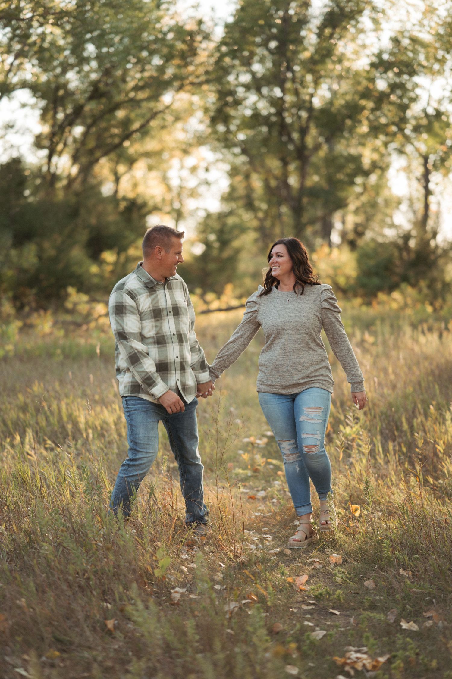 Playful couples session in Brookings SD with couple walking through golden grass with trees in the background.