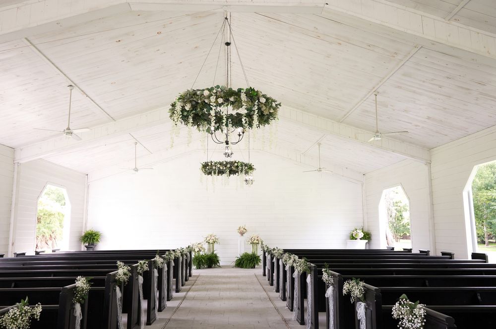 Elegant white chapel with dark wood pews, floral chandelier, and greenery decorations for a wedding ceremony.