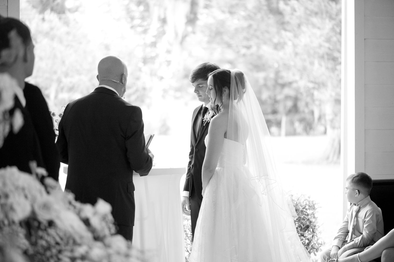 Bride and groom exchange vows during an elegant indoor wedding ceremony in black and white photo.