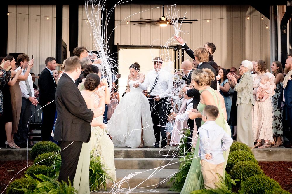 Bride and groom exit wedding reception through cheering guests tossing streamers in festive send-off.