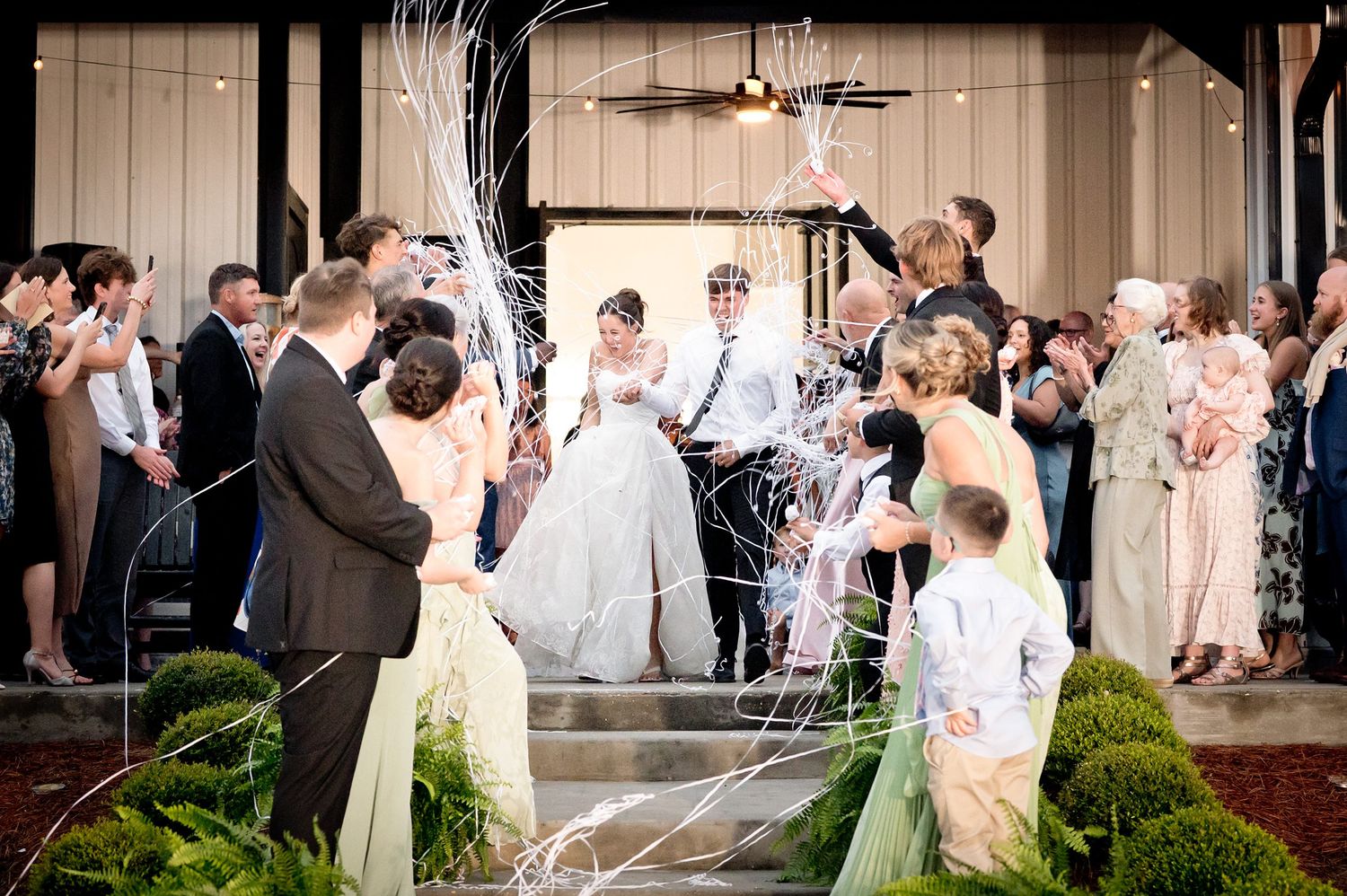 Bride and groom exit wedding reception through cheering guests tossing streamers in festive send-off.