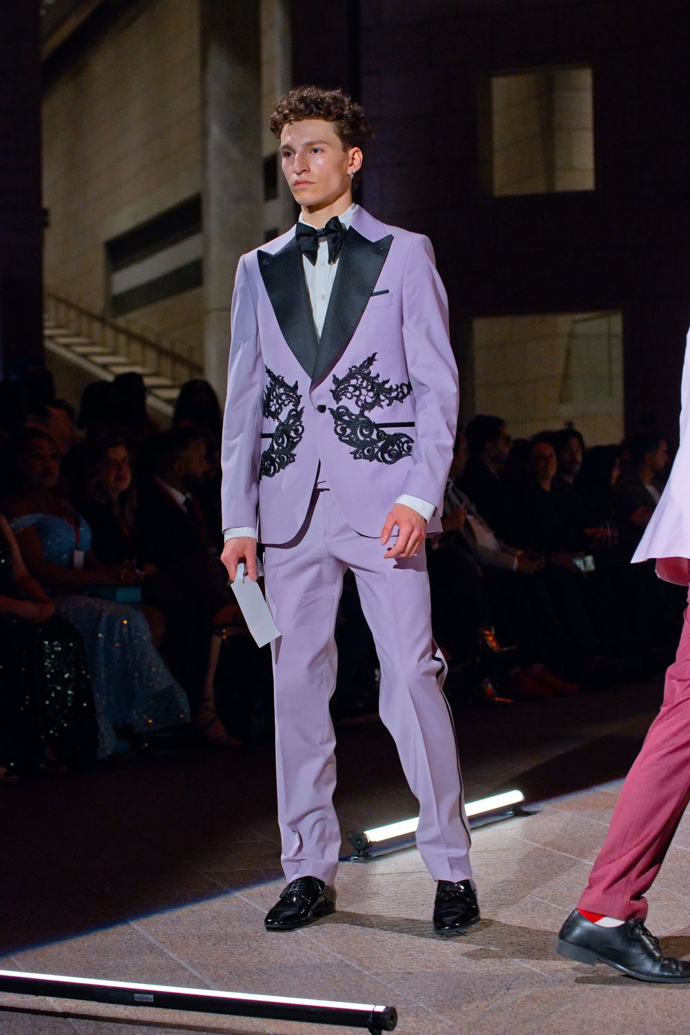 Male model showcases lavender suit with black dragon embroidery and satin lapels on fashion runway.
