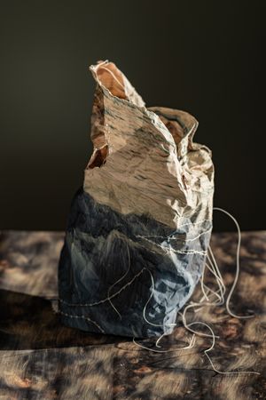 Weathered fabric bag with dark landscape painting, frayed edges, and loose white threads on a rustic wooden surface.