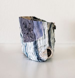 Crumpled blue and white fabric vessel with marbled texture, shaped into an abstract sculptural form on a white surface.