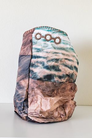 Crumpled fabric backpack with ocean wave print and decorative sun charms on white background.