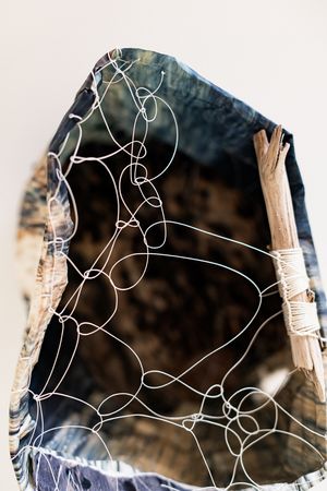 Abstract sculpture with white wire loops over dark fabric supported by wooden sticks.