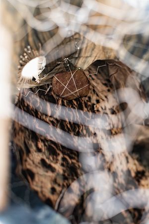 Close-up of a circular wooden disc wrapped in wire mesh, surrounded by natural textures and delicate white feathers.