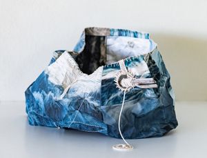 Blue and white crumpled fabric tote bag with decorative rope detail on a white surface.
