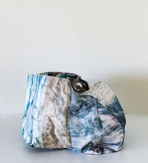 Crumpled fabric vase with blue and white marble-like pattern sitting on a white surface against a light background.