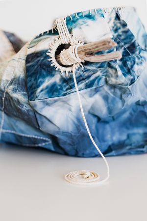 Blue tie-dye fabric bundle with white rope and circular macrame detail on white surface.