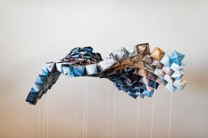 Suspended origami-style sculpture made of blue and brown folded fabric hanging from thin wires.