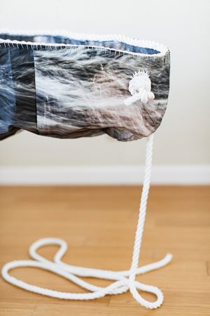 Abstract sculptural bag made from photographic fabric depicting misty landscapes, with a white rope hanging below.
