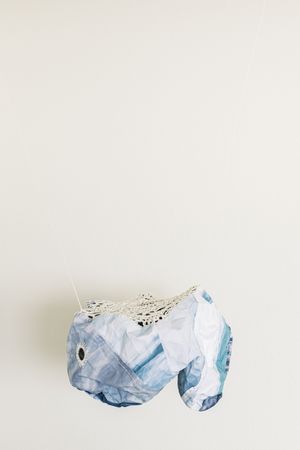 Handmade blue patterned fabric elephant sculpture with white crochet detail mounted on a white wall.