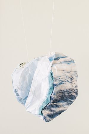 Two crumpled fabric pieces with ocean wave prints in blue and white tones, suspended by white strings against a light background.