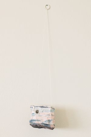 Small handmade hanging planter with blue and pink abstract pattern, suspended by white cord from wall hook.