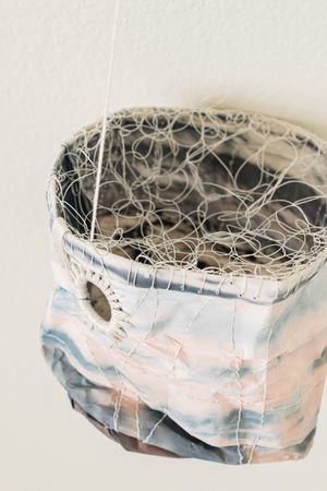 A hanging cylindrical fabric sculpture with intricate wire mesh top and marbled pastel print.