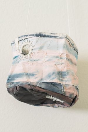 Crumpled fabric pouch with pastel blue and pink tones, featuring circular embellishments and stitched details, hanging by strings.