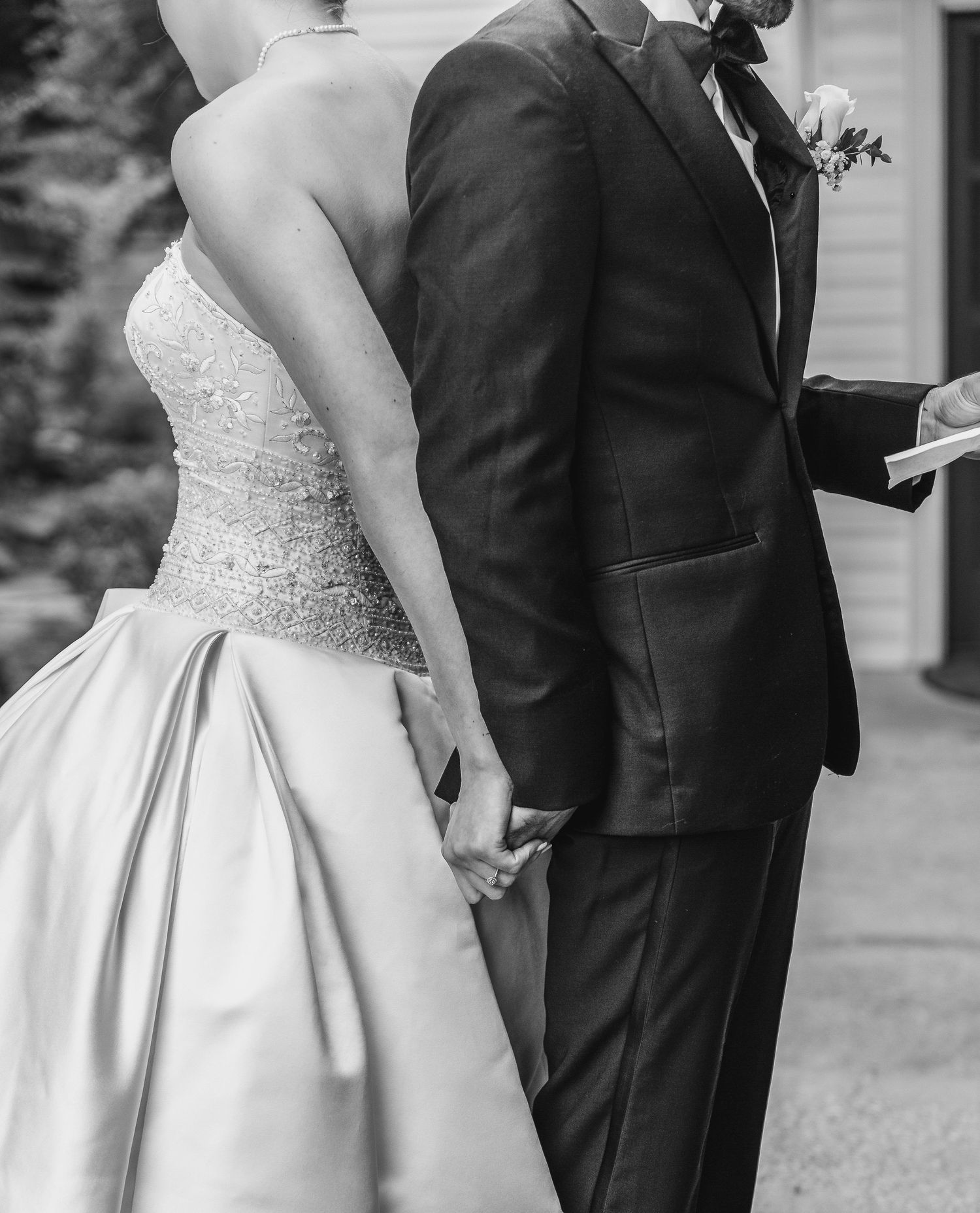 Black and white photo of a bride and groom holding hands during their wedding ceremony outdoors.
