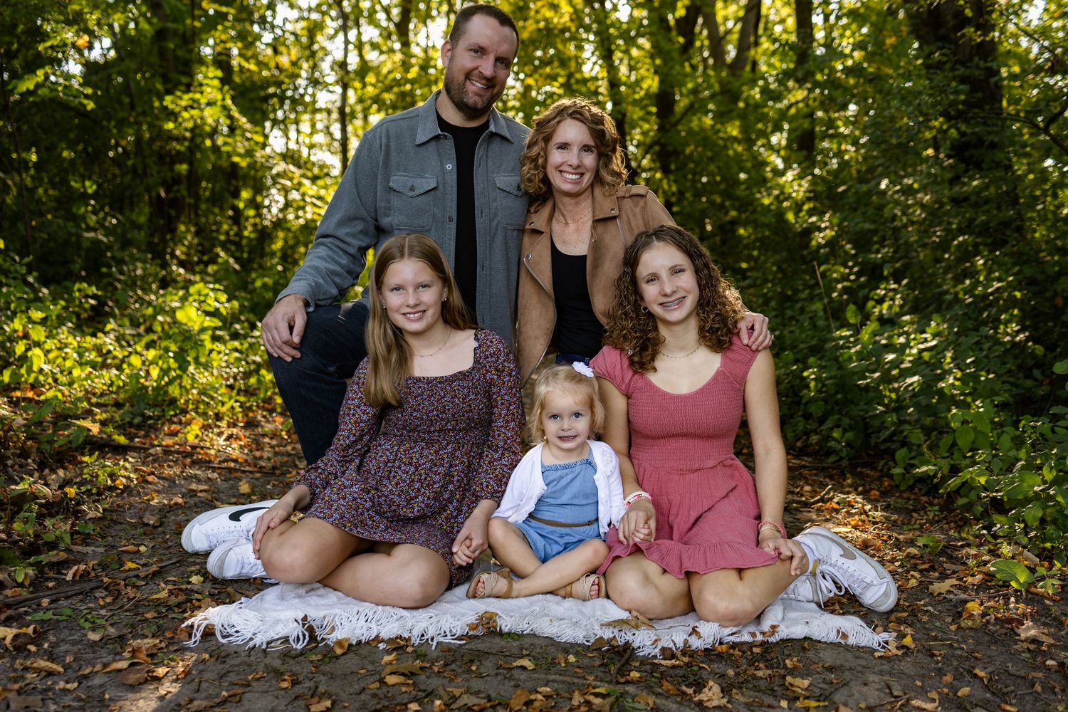 Large family group portrait outdoors near bare tree during autumn sunset in a wooded backyard setting.