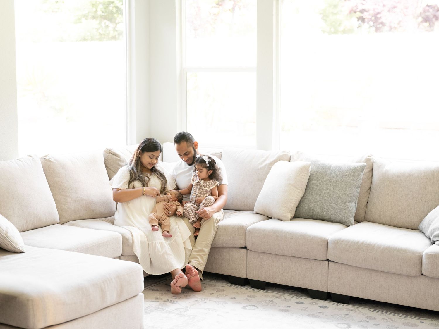 Family of four sitting together on a large cream sectional sofa in a bright, airy living room.