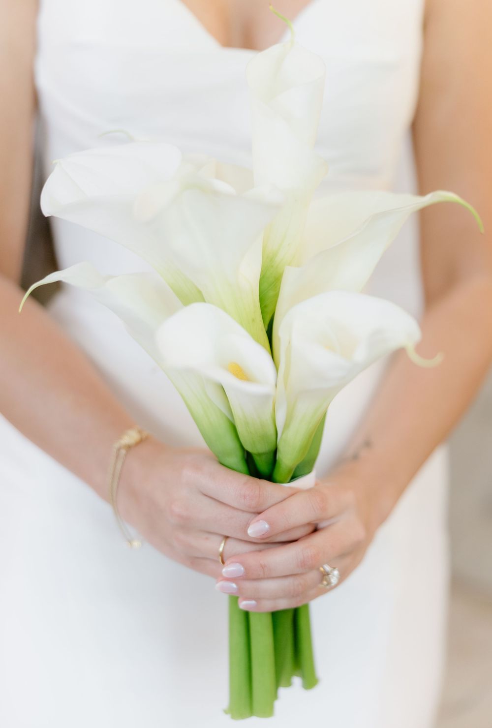 Bride holds an elegant minimalist bouquet of white calla lilies on her wedding day.