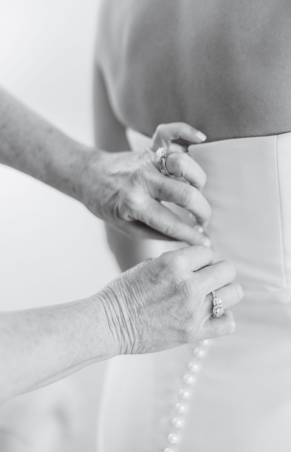 Black and white photo of hands fastening pearl buttons on a wedding dress.
