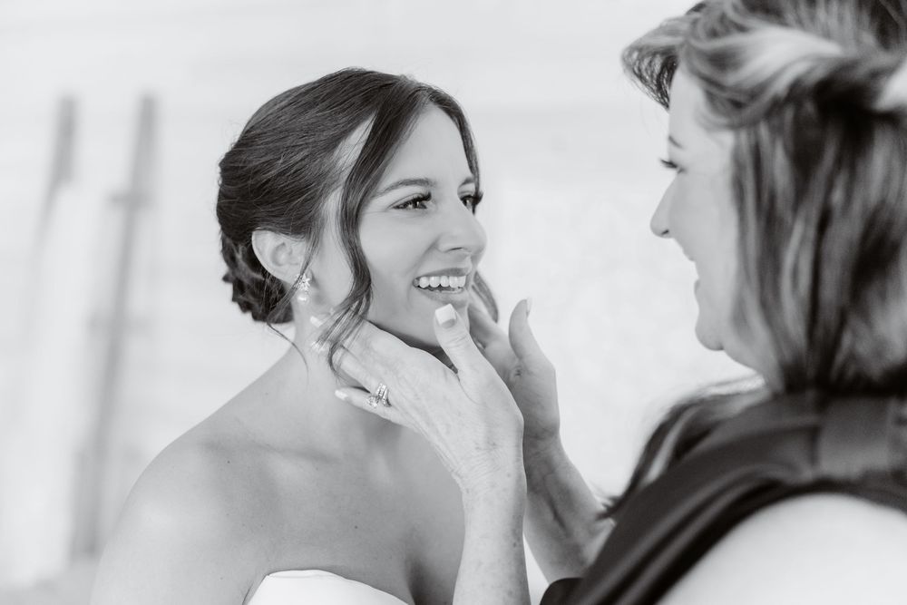 Black and white photo of bride smiling as woman touches her face tenderly.