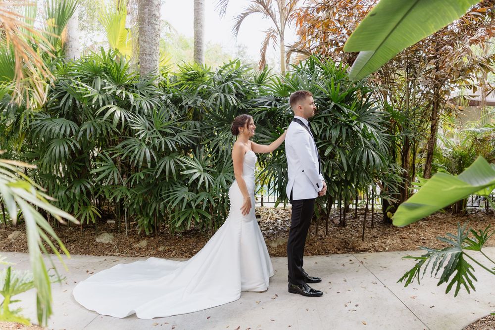 Bride and groom sharing first look moment surrounded by lush tropical greenery outdoors.