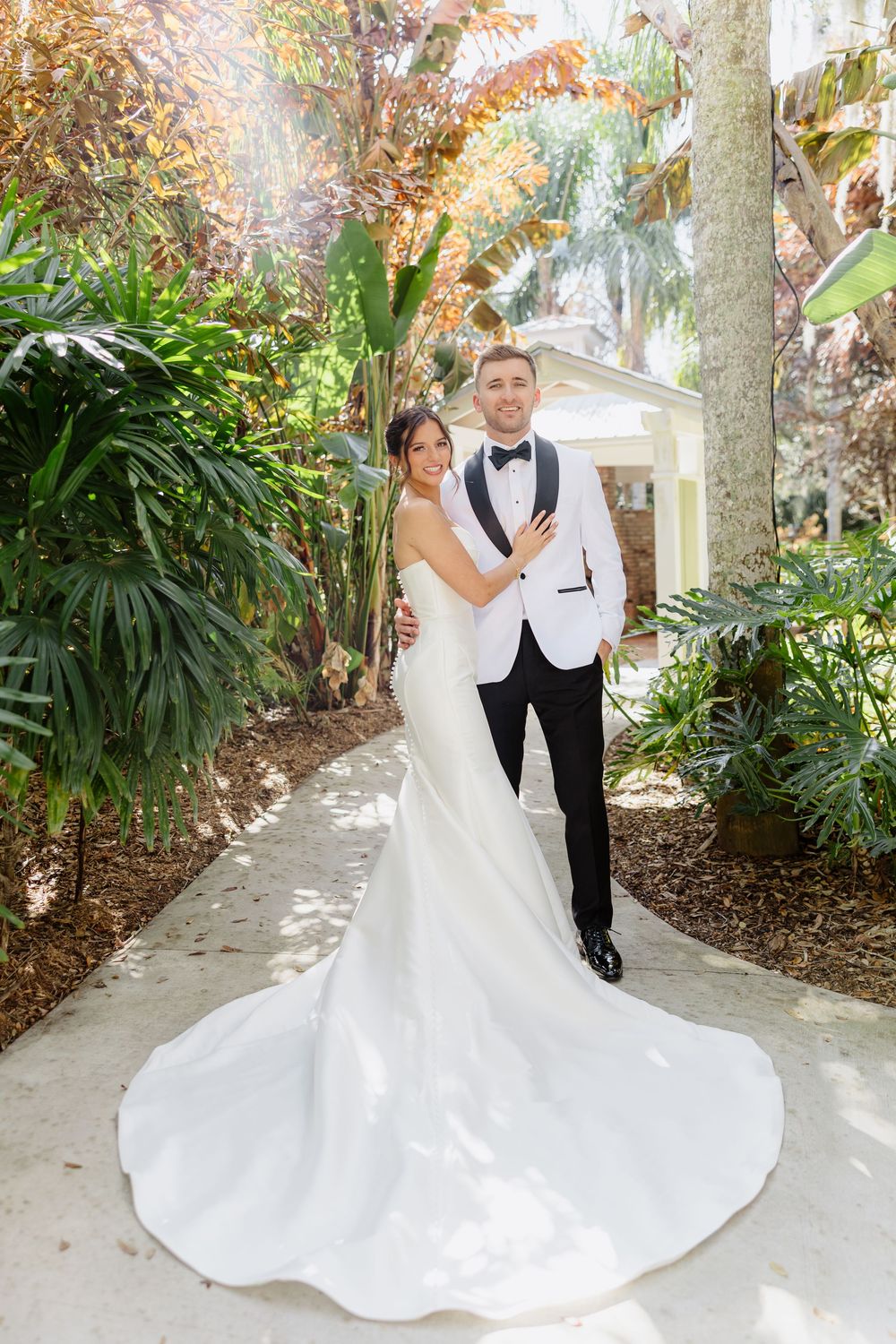 Bride and groom pose in tropical garden, bride wearing stunning long-train white gown.