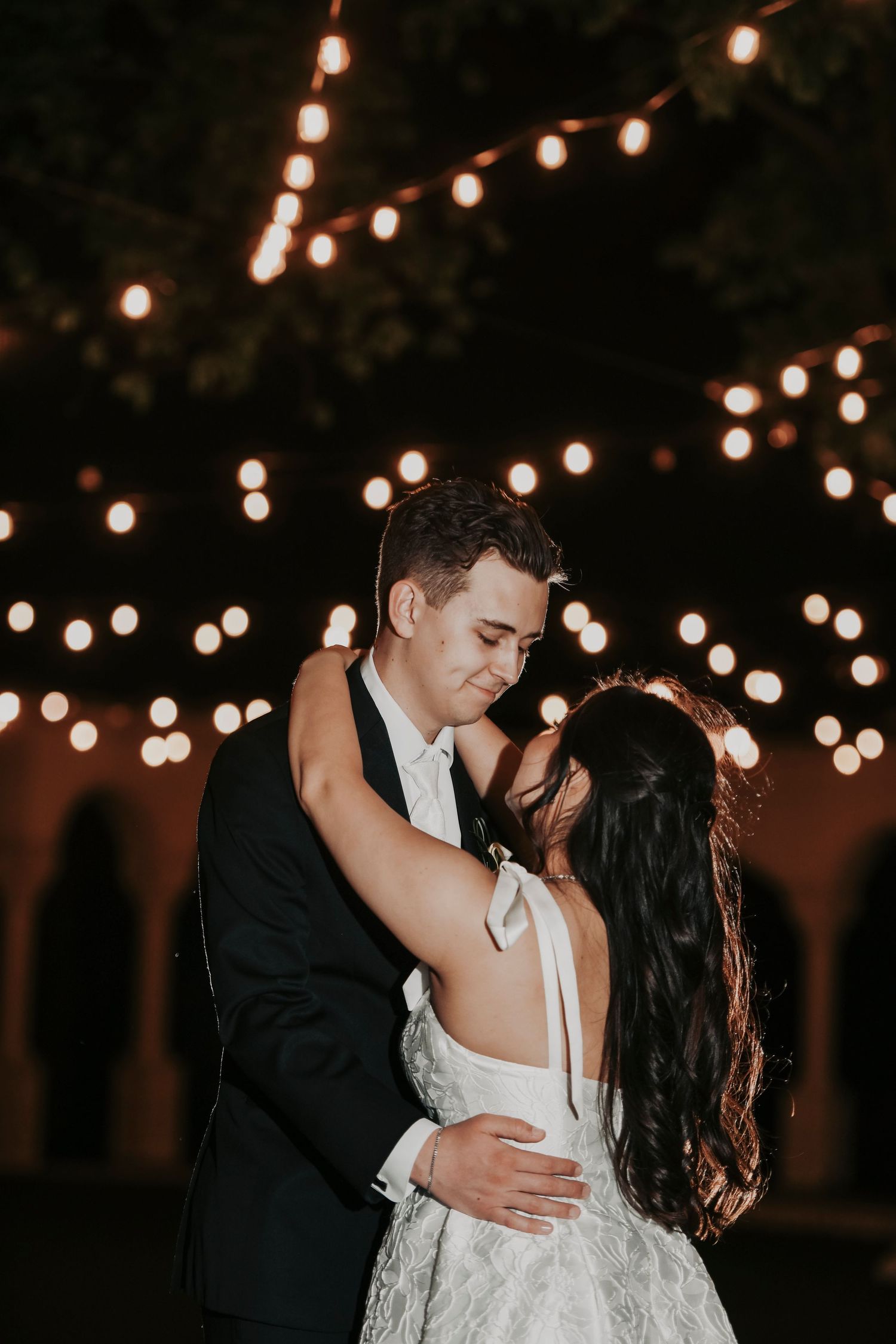 warm twinkling lights sparkle as a bride and groom embrace during their private last dance in aubrey texas