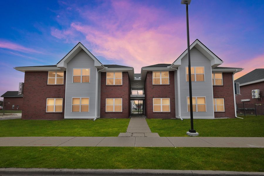 Brick apartment building with manicured lawn under a vibrant sunset sky.