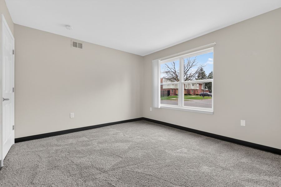 Bright empty bedroom with neutral carpet, beige walls, and a window with natural light.