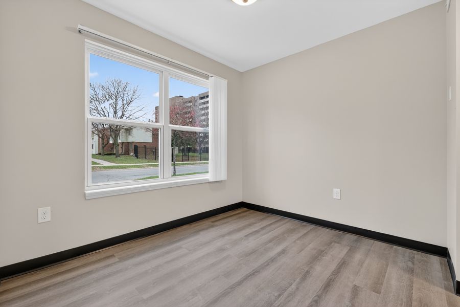Empty room with hardwood floors, neutral walls, and a large window overlooking a residential street.
