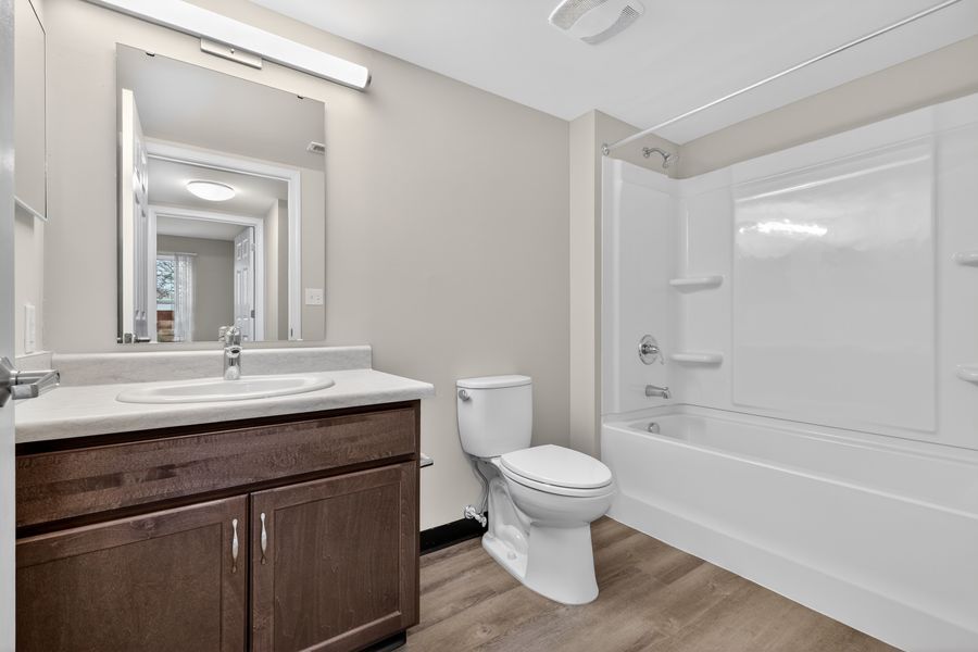 Modern bathroom with dark wood vanity, white toilet, and bathtub-shower combo with light wood-look flooring.