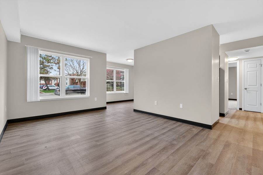 Bright empty living room with hardwood floors, neutral gray walls, and large windows allowing natural light.