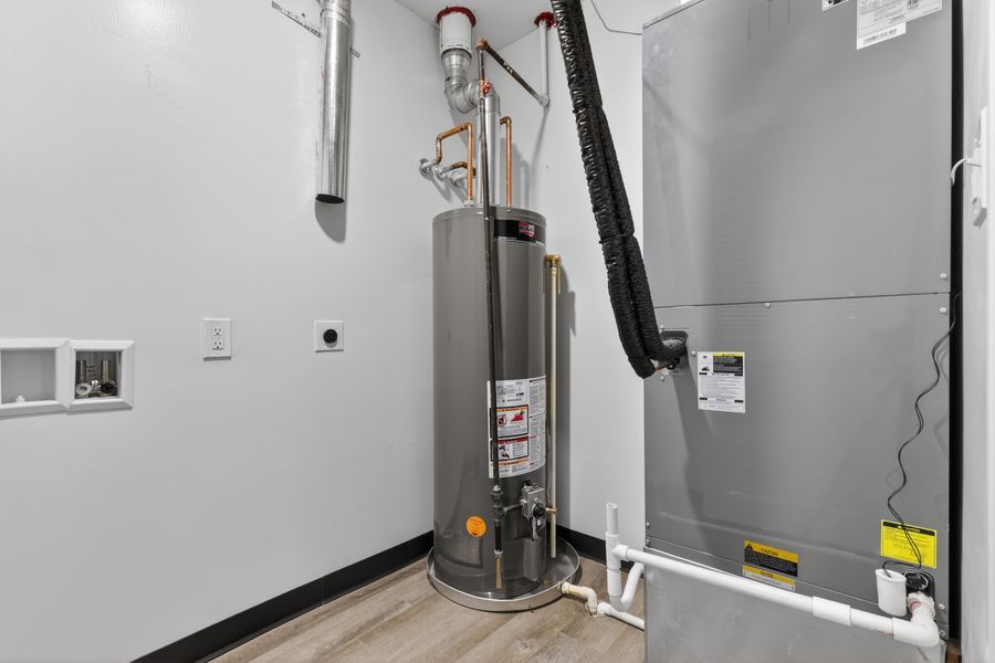 Utility room featuring a water heater and HVAC system with ductwork on hardwood flooring.
