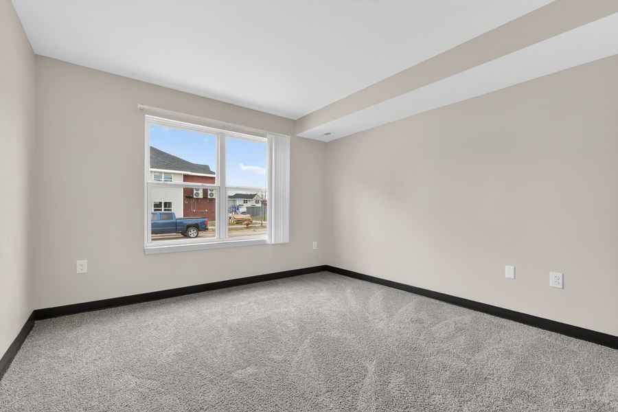 Bright empty bedroom with carpet flooring and a large window with natural light.