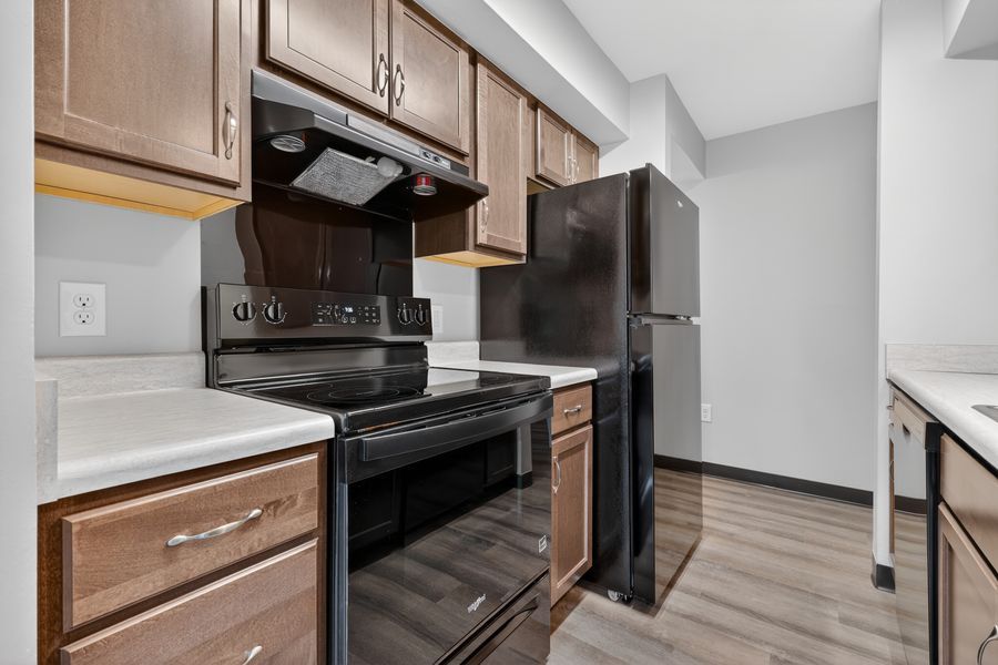 Modern kitchen with brown cabinets, black appliances, electric range, and hardwood-style flooring.