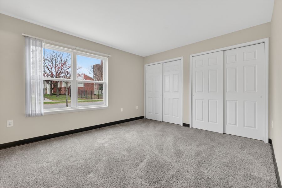 Bright bedroom with gray carpet, two white closets, and a large window with natural light.