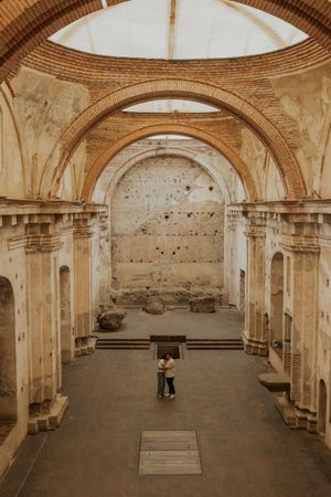Couple embracing inside ancient ruined church with brick arches and open sky ceiling in Antigua, Guatemala.