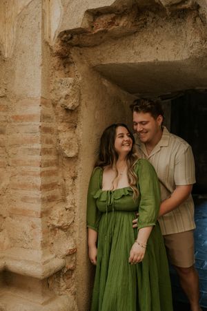 A smiling couple poses in a rustic stone archway, the woman in a green dress and man in a striped shirt.