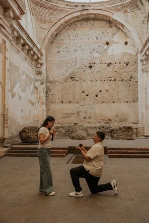 Man proposes on one knee to woman inside ancient stone ruins with arched walls in Antigua, Guatemala.