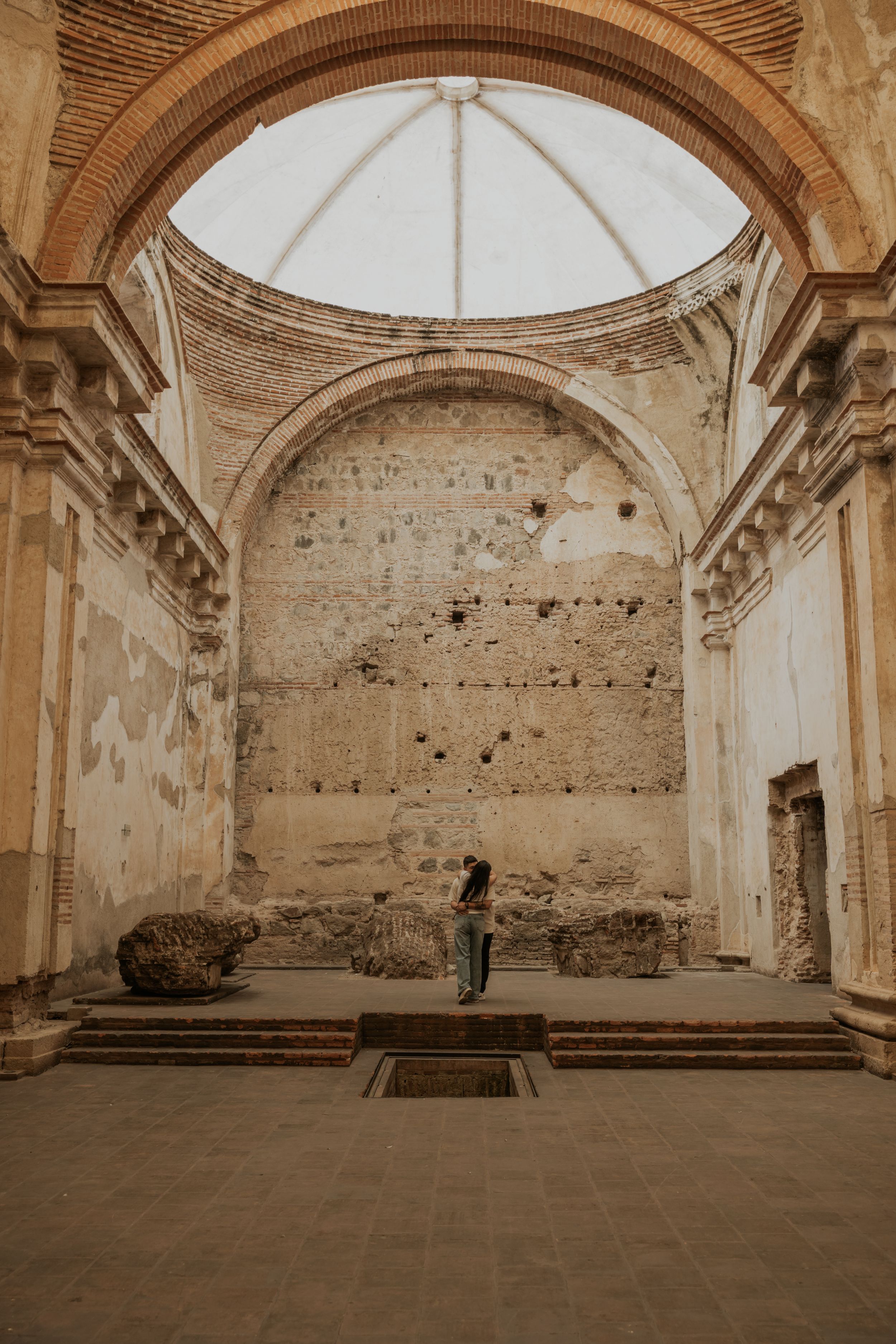 Person standing inside ancient ruined church with grand arch, dome, and weathered stone walls in Antigua, Guatemala.