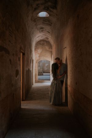 Couple sharing a romantic embrace in a dimly lit ancient stone corridor with arched ceilings.