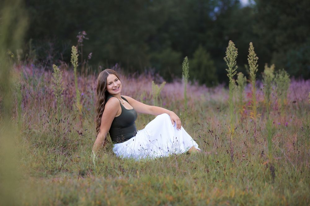 Senior portrait at Island Lake, Brighton Michigan; girl sitting in flower field with cinematic aesthetic by South Lyon, MI photographer