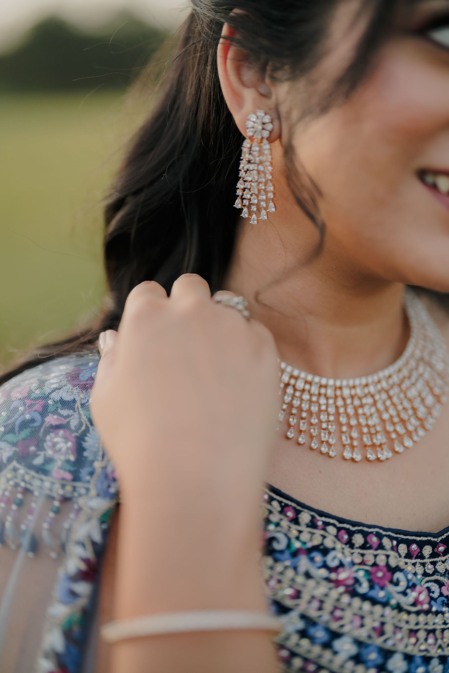 Close-up of Indian bride wearing sparkling diamond chandelier earrings, choker necklace, and bracelet in traditional attire.
