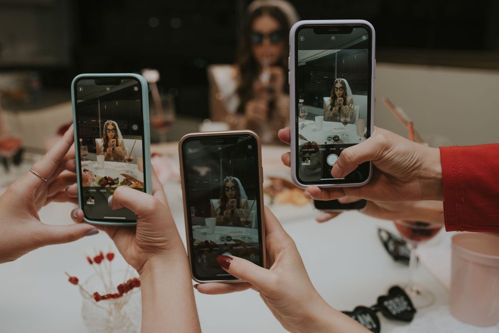 Multiple hands hold up phones to capture a moment at a social gathering.